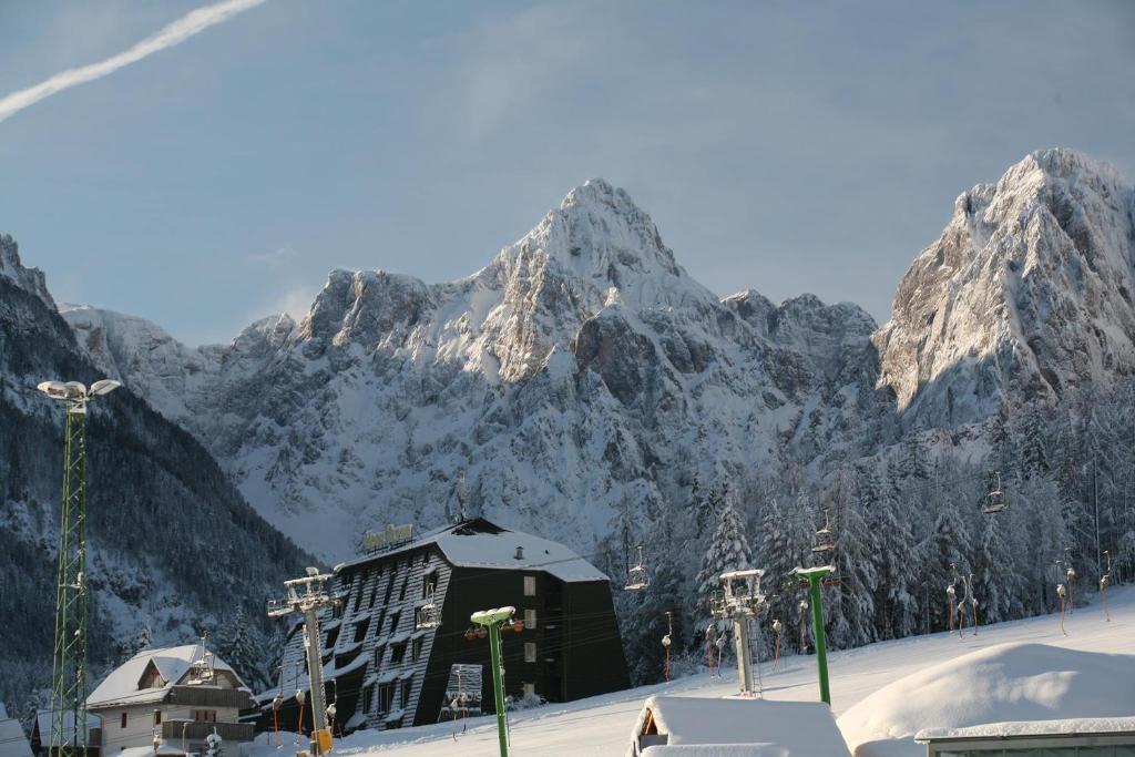 een met sneeuw bedekte berg met een gebouw ervoor bij Hotel Alpina in Kranjska Gora