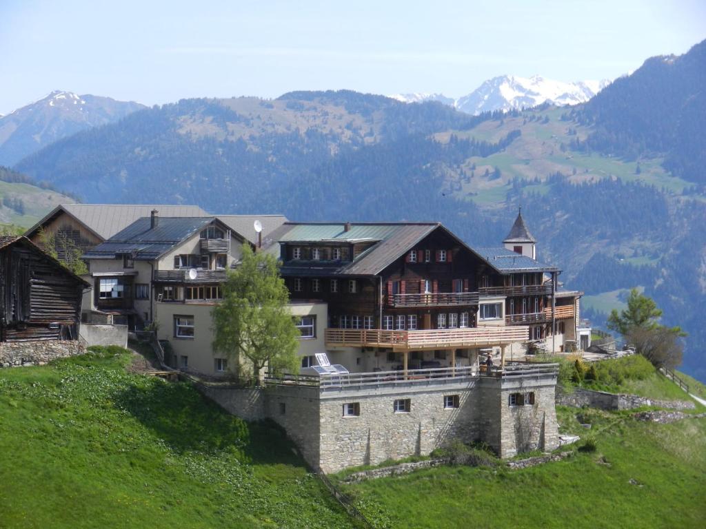 une grande maison sur une colline avec des montagnes en arrière-plan dans l'établissement Hotel Restaurant Capricorns, à Wergenstein