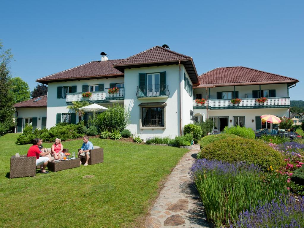 un grupo de personas sentadas en el césped frente a una casa en Villa Konstanze, en Velden am Wörthersee