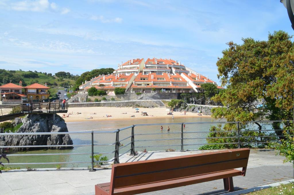 un banc en face d'une plage avec un bâtiment dans l'établissement Playa De Arnadal Isla, à Isla