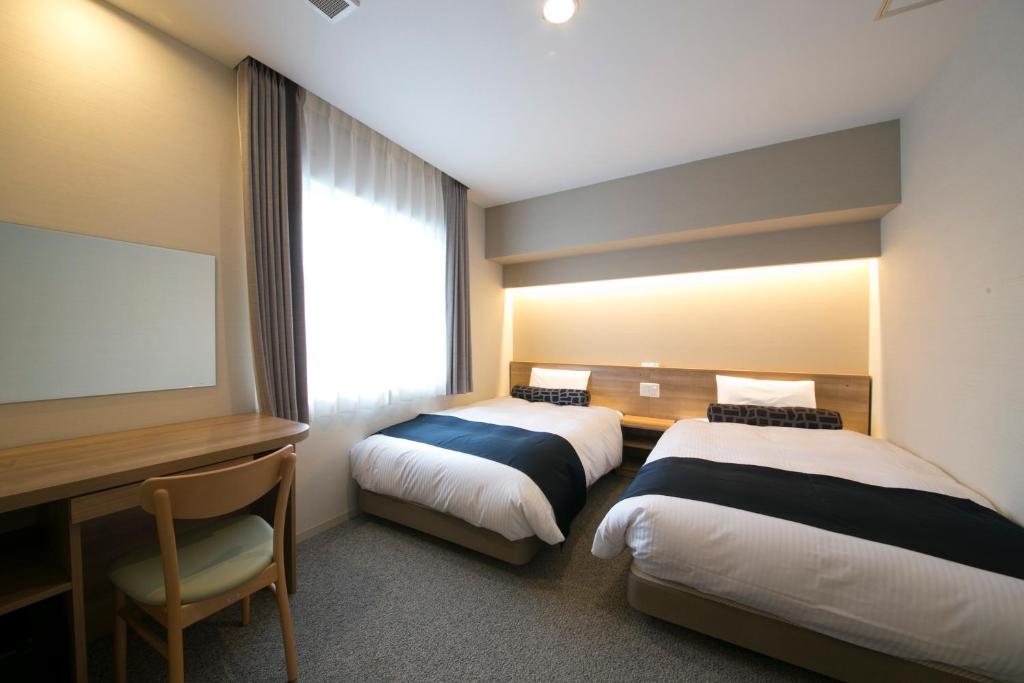 ein Hotelzimmer mit 2 Betten, einem Schreibtisch und einem TV in der Unterkunft Just Inn Premium Nagoya Station in Nagoya