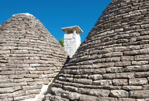 dois grandes telhados de pedra com um monumento ao fundo em Trullo Giardino Fiorito em Alberobello