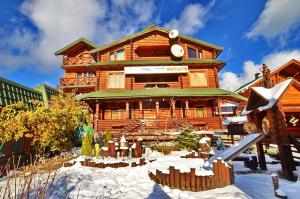 une grande maison en bois avec de la neige devant elle dans l'établissement Urochyshe Vyshnya, à Bukovel