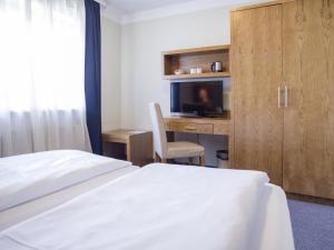 Hotel Königstein Kiel by Tulip Inn في كيل: غرفة فندقية بسرير ومكتب مع تلفزيون