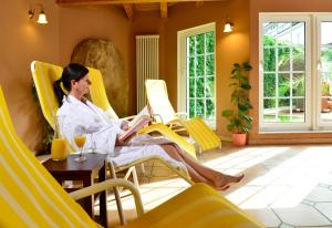 une femme assise sur une chaise jaune en lisant un livre dans l'établissement Hotel Der Lindenhof, à Gotha