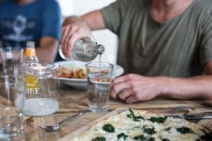 Ein Mann schüttet Wasser in ein Glas auf einen Tisch mit einer Pizza. in der Unterkunft Beach Apartments Heiligenhafen in Heiligenhafen