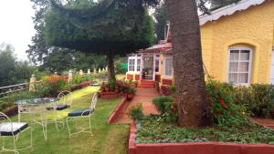 een geel huis met stoelen en een boom in de tuin bij Wyoming Heritage in Ooty