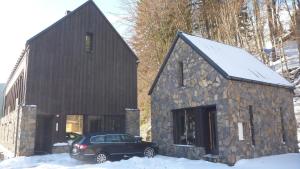 un'auto parcheggiata di fronte a una casa in pietra nella neve di Krakonošova Dílna "WOODHAUS" a Špindlerův Mlýn