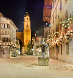 een stadsstraat met 's nachts een klokkentoren bij Post-Hotel in Mittenwald