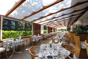 een restaurant met witte tafels, stoelen en ramen bij Suite Erica Lignano Hotel in Lignano Sabbiadoro