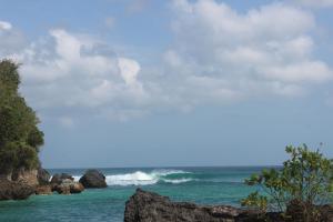 a wave in the ocean with rocks in the foreground at Adi Bali Homestay in Uluwatu