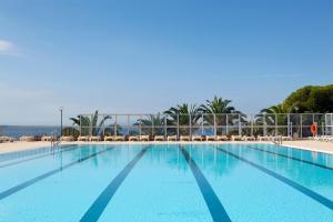 ein großer blauer Pool mit Stühlen und das Meer in der Unterkunft Almadraba Park Hotel in Roses