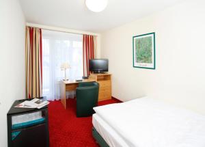 a hotel room with a bed and a desk with a television at Hotel Biederstein am Englischen Garten in Munich