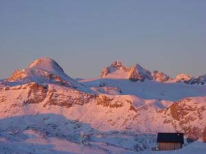 une montagne enneigée avec une maison au premier plan dans l'établissement Dormio Gasthof Höllwirt, à Obertraun