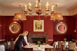 een vrouw in een eetkamer met tafels bij Ockenden Manor Hotel & Spa in Cuckfield