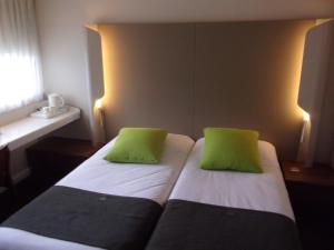 a bed with two lime green pillows on it at Campanile Hotel Chantilly in Chantilly