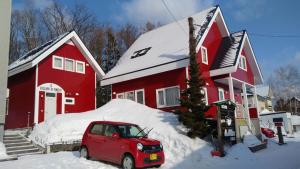 una casa rossa con un'auto rossa parcheggiata nella neve di Cottage Morino Nakamatachi a Furano