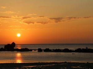 a sunset over the ocean with rocks in the water at Scallop Beach Condominium in Onna