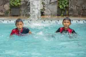 twee jonge jongens zwemmen in een zwembad met een fontein bij KHAS Semarang Hotel in Semarang