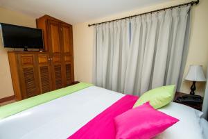 een slaapkamer met een bed met roze en groene kussens bij Hotel Colibri in Managua