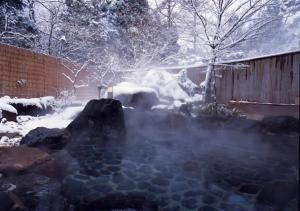 een warmwaterbron met sneeuw in een tuin met een hek bij Higashiyama Park Hotel Shinfugetsu in Aizuwakamatsu