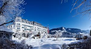 um edifício coberto de neve em frente a um lago em Grand Hotel Zell am See em Zell am See