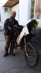 un hombre está de pie junto a una motocicleta en Guest House Sharq 21, en Khujand