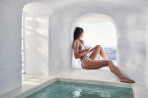 une femme assise sur un rebord de fenêtre à côté d'une piscine dans l'établissement Limestone, à Fira