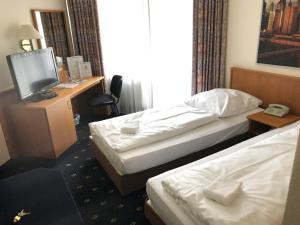 a hotel room with two beds and a desk with a television at Karaman Group Hotel in Bad Nenndorf