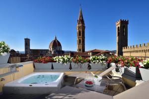 una terraza en la azotea con bañera de hidromasaje y flores en San Firenze Suites & Spa, en Florencia