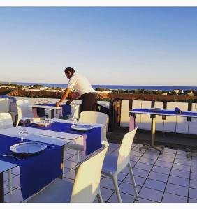 Ein Mann steht auf einem Balkon mit Tischen und Stühlen in der Unterkunft L'Angolo Di Beppe in Torre Lapillo