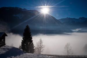 un soleil se levant au-dessus d'une montagne couverte de brouillard et d'un lac dans l'établissement Ferienwohnung Steiner, à Wald im Pinzgau