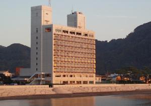 un grand bâtiment sur la plage avec des montagnes en arrière-plan dans l'établissement Nishiizu Matsuzaki Itoen Hotel, à Matsuzaki