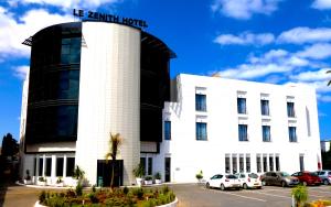 un grande edificio bianco con auto parcheggiate in un parcheggio di Le Zenith Hotel Oran a Orano