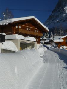 dom pokryty śniegiem obok drogi pokrytej śniegiem w obiekcie Chalet Verbrunnenhaus Grindelwald w mieście Grindelwald