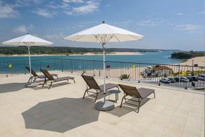 a group of chairs and umbrellas on a patio near the water at Cerca da Vitoria 3 Milfontes in Vila Nova de Milfontes