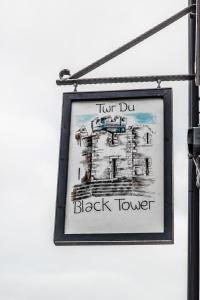 una señal colgando de un poste con una torre de bloqueo en The Black Boy Inn, en Caernarfon