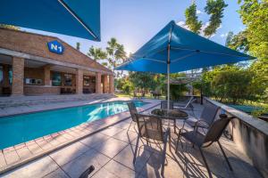 un patio con mesa y sombrilla junto a la piscina en N1 Hotel & Campsite Victoria Falls, en Victoria Falls