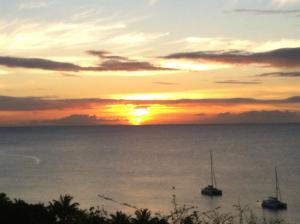 a sunset over the ocean with boats in the water at Breeze Cottage in Five Islands Village