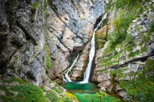 une cascade dans un canyon avec de l'eau verte dans l'établissement Apartment Sonce, à Bohinj