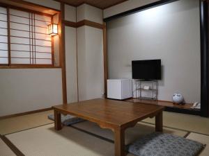 ein Wohnzimmer mit einem Holztisch und einem TV in der Unterkunft Kimatsu Ryokan in Hiroshima