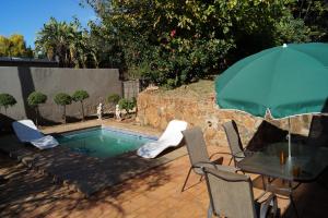 - une piscine avec une table, des chaises et un parasol dans l'établissement Westmoreland Lodge, à Johannesbourg