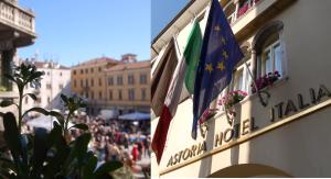 Eine Gruppe von Menschen, die eine Straße entlang gehen, mit Flaggen auf einem Gebäude in der Unterkunft Astoria Hotel Italia in Udine