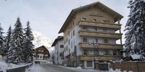 een groot gebouw aan de kant van een met sneeuw bedekte weg bij Albergo Genziana in San Vigilio Di Marebbe