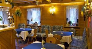 een restaurant met 2 tafels, stoelen en ramen bij Albergo Genziana in San Vigilio Di Marebbe