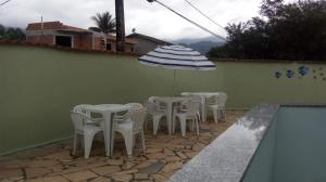 d'une terrasse avec des tables et des chaises blanches ainsi qu'un parasol. dans l'établissement Chale Cantinho Albamar, à Ubatuba