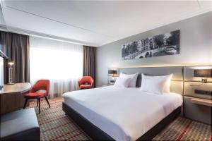 Ramada by Wyndham Amsterdam Airport Schiphol في باتهوفيدورب: غرفة فندقية بسرير كبير وكراسي حمراء