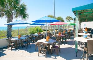 un patio al aire libre con mesas, sillas y sombrillas en Oceanfront Litchfield Inn, en Pawleys Island