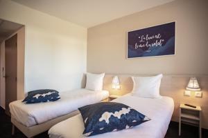 two beds in a hotel room with a painting on the wall at Ace Hôtel Toulouse Blagnac in Cornebarrieu