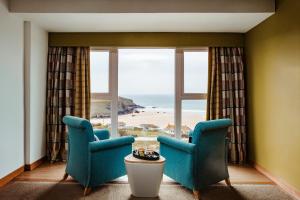 een kamer met 2 stoelen en een groot raam met een strand bij Bedruthan Hotel & Spa in Newquay